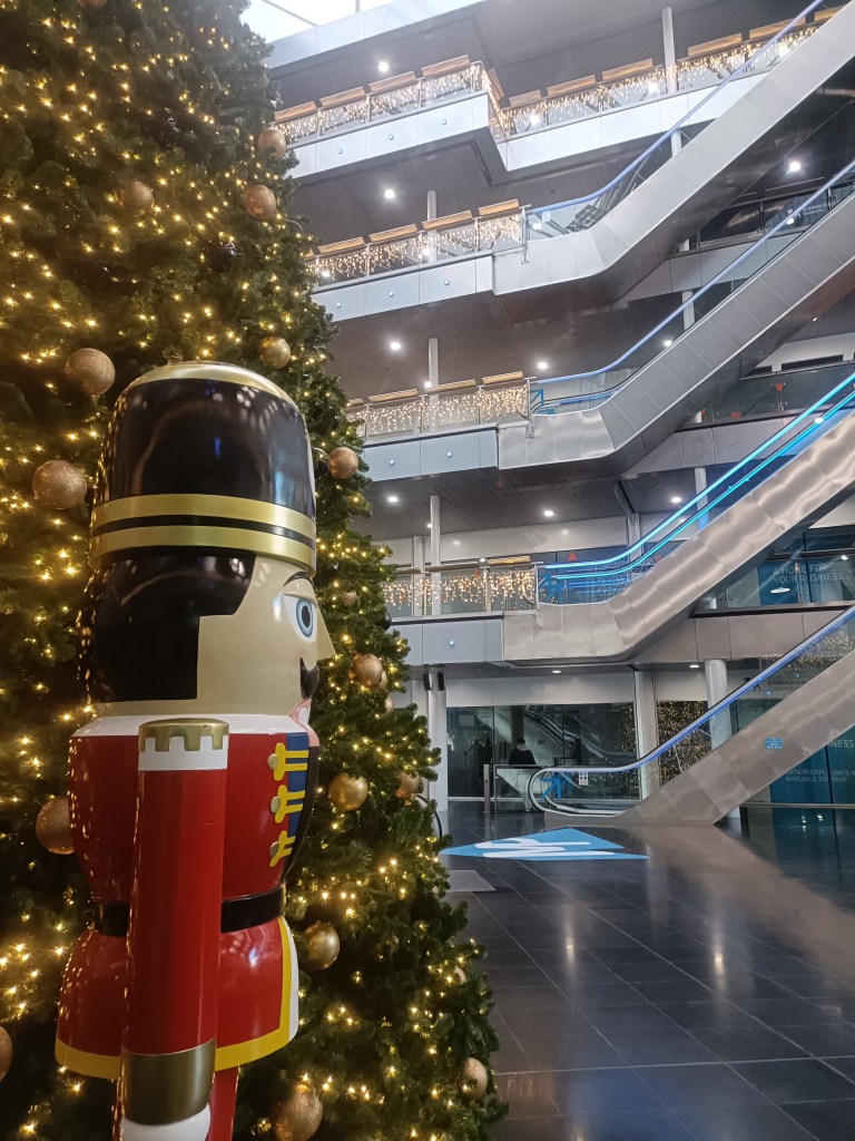 A giant soldier toy by a chritmas tree in a huge building